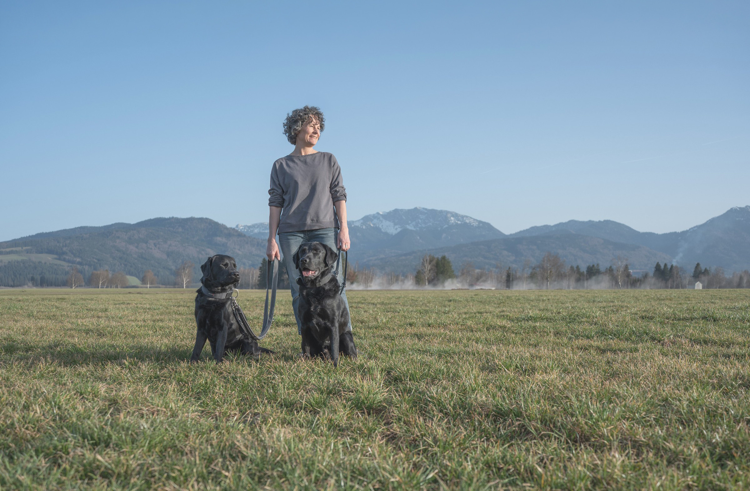 Eva-Maria Pitman mit zwei Hunden in der Natur, MittenKraft Mensch-Hund-Begleitung, Führung aus Klarheit, Beziehung und Kommunikation